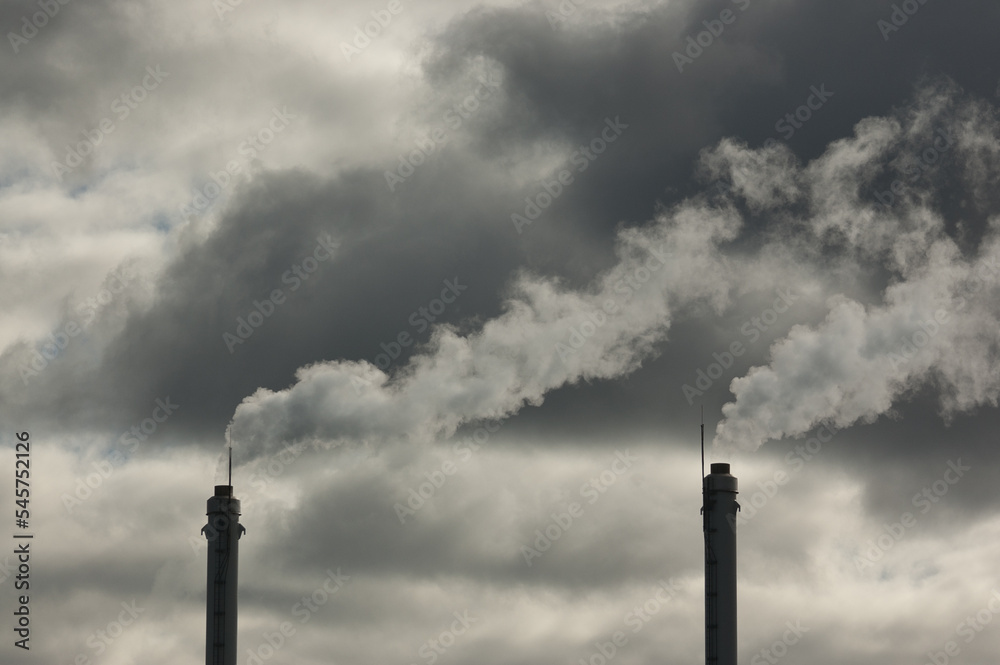 metal pipes of the plant against a gray sky, gray smoke comes out of the pipes