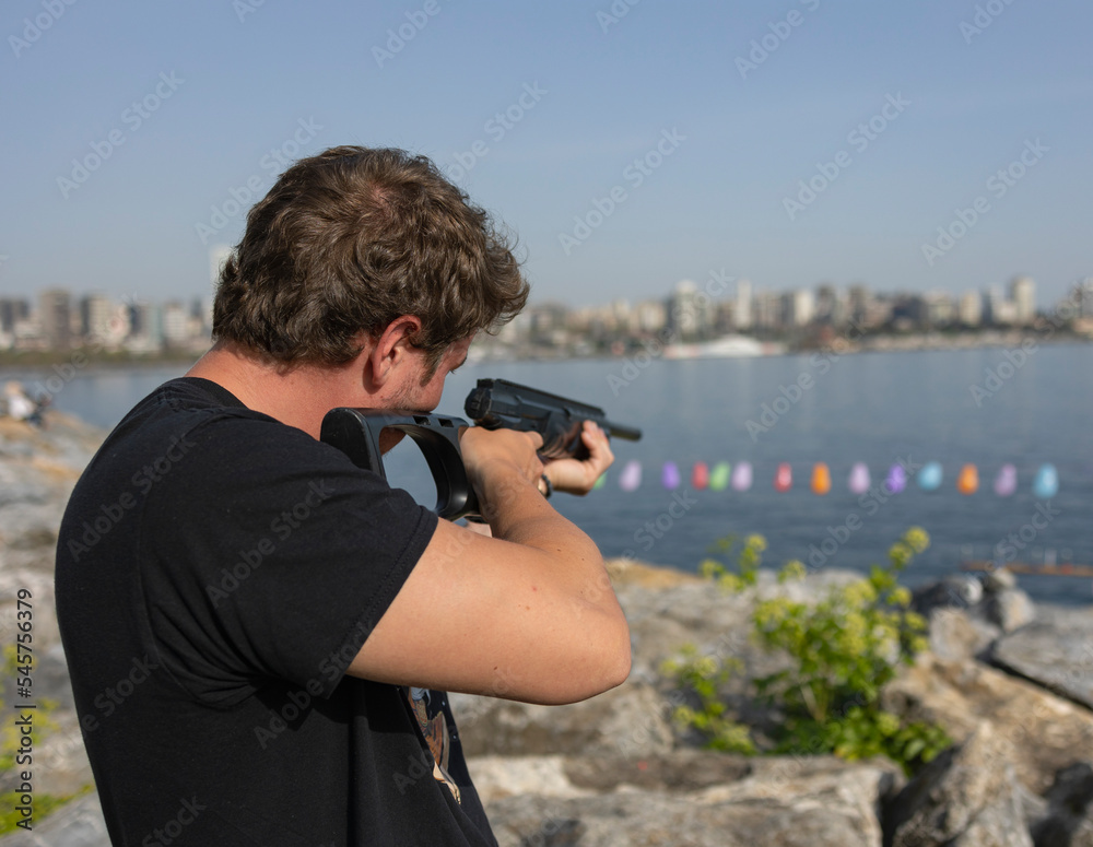 A Man Shooting With Gun At Balloons on Background With Sea.