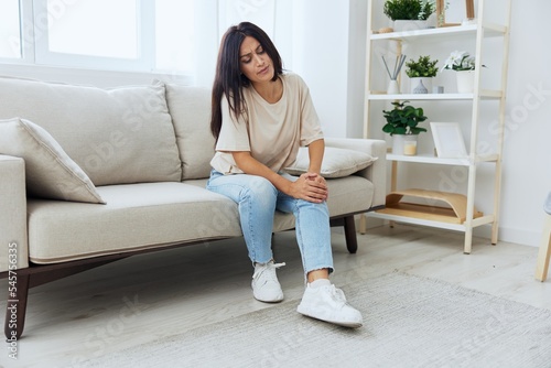Woman sitting on the couch at home leg and foot pain, sprain and muscle strain, leg injury