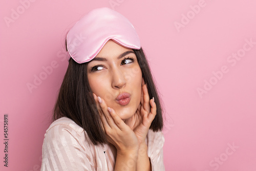 Porter is a beautiful young woman of oriental appearance standing in pink pajamas and a sleeping mask in the bedroom. suffers from insomnia.