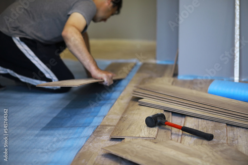Installing laminated floor, detail on man hands blue wooden tile, over white foam base layer, small pile with more tiles background