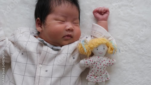 産後1か月0歳の新生児が女の子の人形と一緒に寝ているやや左寄りの動画 photo
