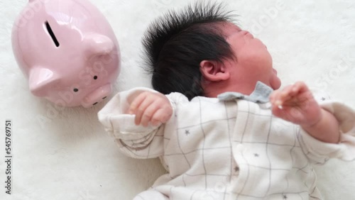 産後1か月0歳の新生児の左隣りに豚の貯金箱を配置した動画 photo