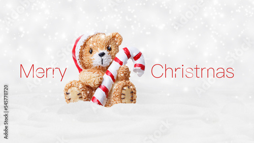 Merry Christmas text and teddy bear with red hat and candy striped cane stick isolated on snowing background, white Christmas concept template for greeting gift card or promotion advertising banner © amedeoemaja