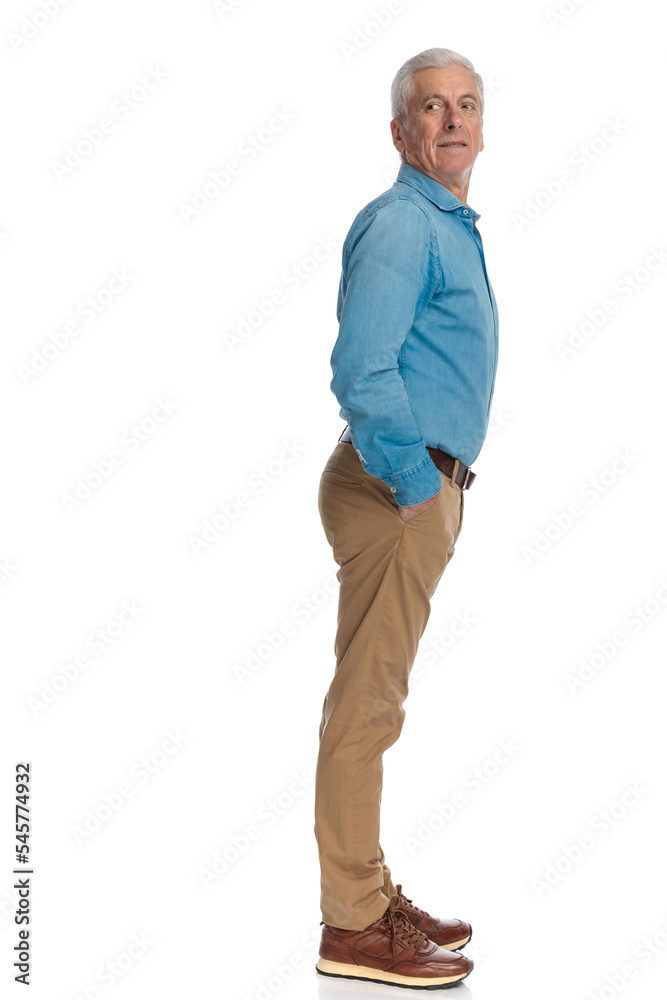 Naklejka premium old man with grey hair holding hands in pockets and looking behind