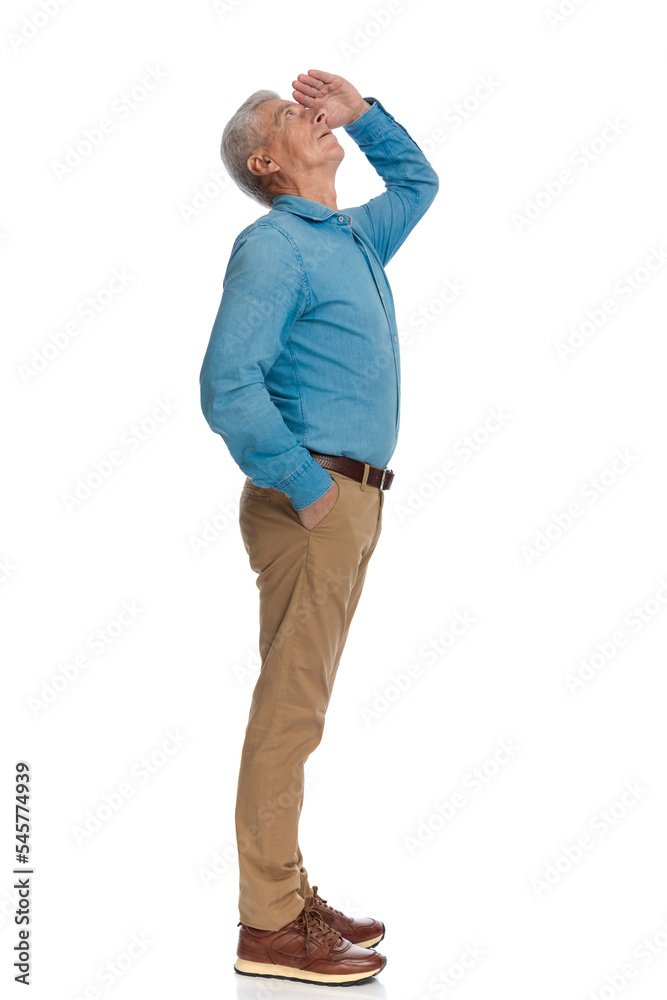side view of man in his 60s holding hand to forehead and looking far away side view of man in his 60s holding hand to forehead and looking far away
