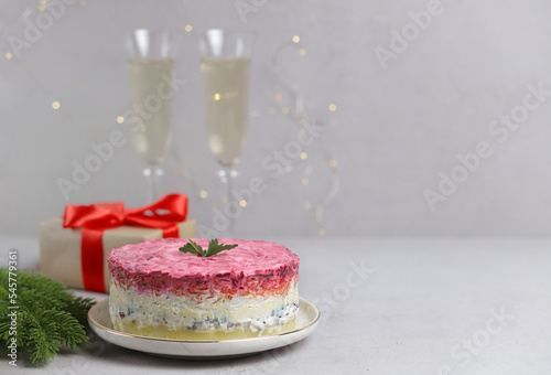 Traditional Russian salad. Layered herring salad under a fur coat on a white plate on a gray background. Russian national cuisine. Selective focus. Copy Space