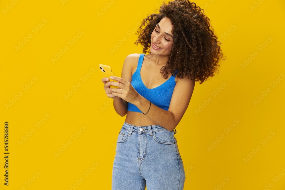 Influencer woman with phone in hand taking selfies talking on video call freelancer social media technology work, with curly afro hair in blue shirt yellow background , smile with teeth, copy space Influencer woman with phone in hand taking selfies talking on video call freelancer social media technology work, with curly afro hair in blue shirt yellow background , smile with teeth, copy space