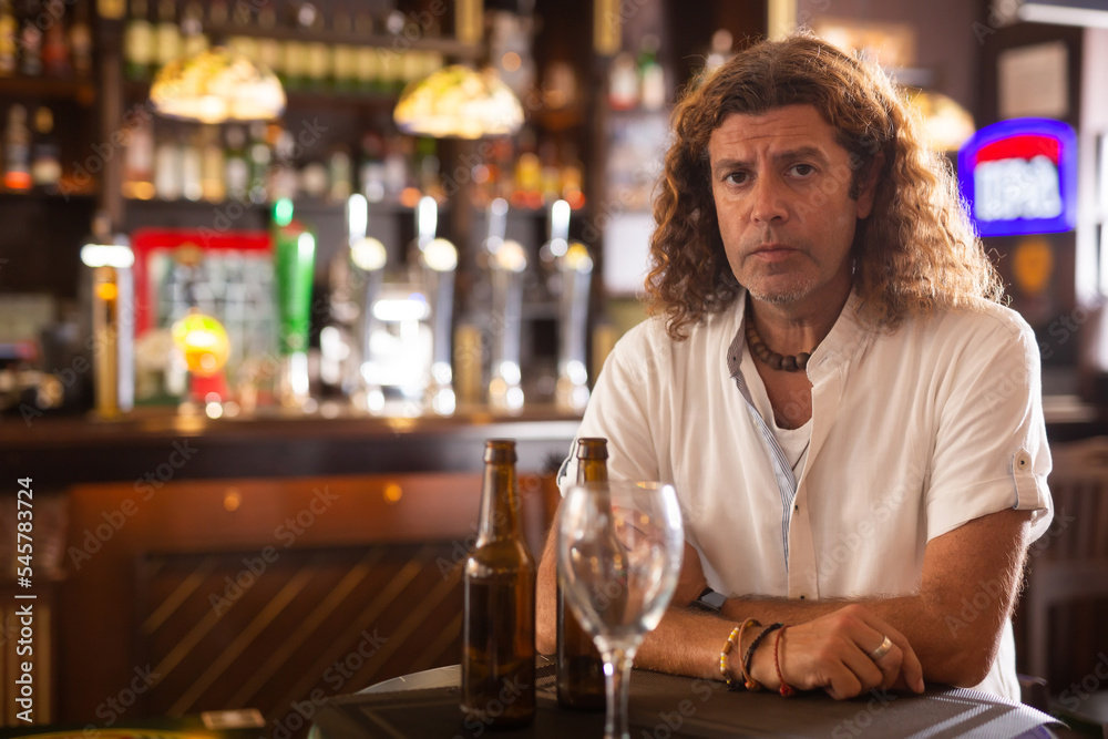 Portrait of handsome man with long curly hair standing at table in pub.