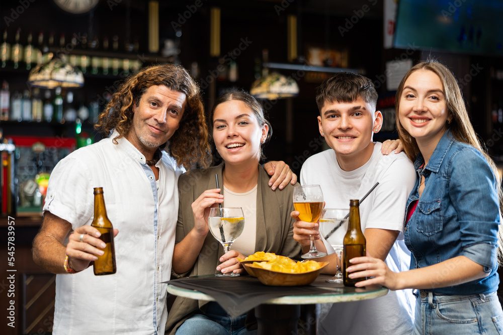 Group photo of cheerful friends meeting at bar, dirinking beer, looking at camera and smiling.
