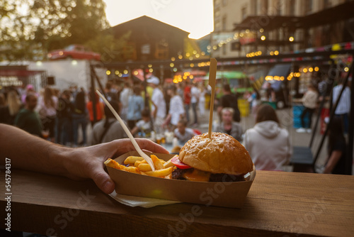 Man hands holding street food burger with french fries on craft paper. Street fast food. festival background photo
