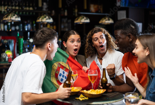 Excited young adult football fans having fun in sports bar, celebrating victory of favorite Portuguese team together after watching match