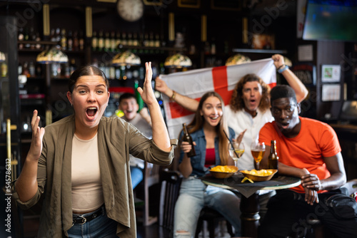 Excited diverse soccer fans with flag of England, rejoicing winning game with glasses of beer and chips in the pub