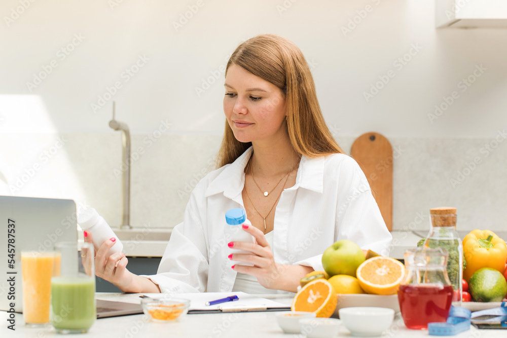 A nutritionist holds jars of vitamins in front of a laptop while sitting at a table A nutritionist holds jars of vitamins in front of a laptop while sitting at a table