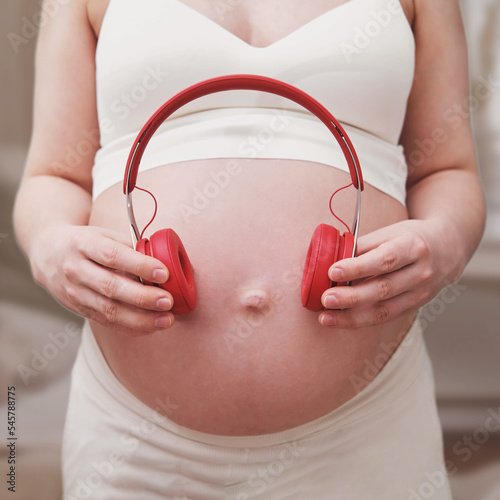 Pregnant woman with music headphones in hand, home living room