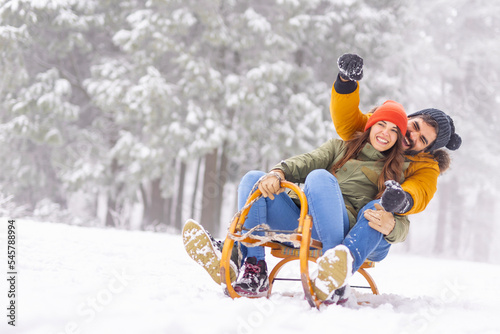 Fotografie Couple sitting on sled and sliding down the hill while on winter vacation