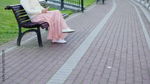 Wallpaper Mural female pink dress white coat sit city park bench using smartphone then put mobile into pocket stand up and go away walk on camera footpath red piles. Loneliness alone woman concept Torontodigital.ca