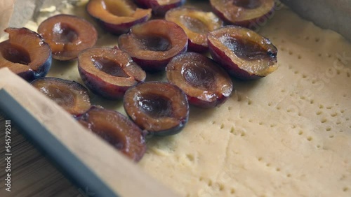 Putting plums on a raw dough in a baking tray for a plum tart , close-up. Homemade pie with ripe and soft plums. 
 