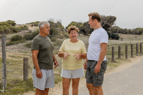 Elderly parents with an adult son walk in the park, communication and care for loved ones © Enigma