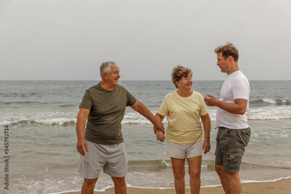 Elderly parents with an adult son walking by the sea, a healthy lifestyle, taking care of the family, Happy family posing at the beach on a sunny day