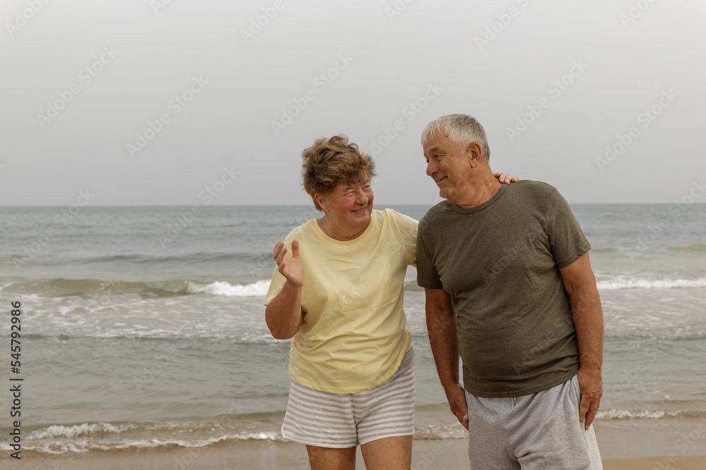 Happy senior couple walking on the beach in a sunny day. Smiling mature couple looking at each other on beach with copy space. Retired man in love with his wife relaxing during vacation. Happy senior couple walking on the beach in a sunny day. Smiling mature couple looking at each other on beach with copy space. Retired man in love with his wife relaxing during vacation.