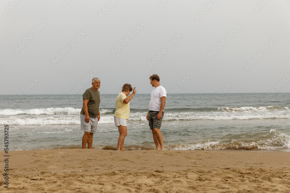 Elderly parents with an adult son walking by the sea, a healthy lifestyle, taking care of the family