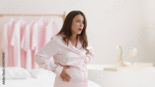 Pregnancy problems. Young pregnant woman suffering from acute stomach pain, holding her belly and frowning, free space