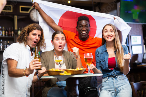 Diverse men and women supporting Japan sports team in pub together. Happy group of friends raising Japan flag.