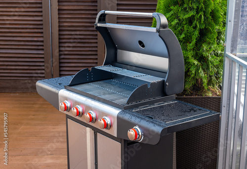 Close-up of modern grill. Wooden outdoor terrace of luxury private house. Green tree.