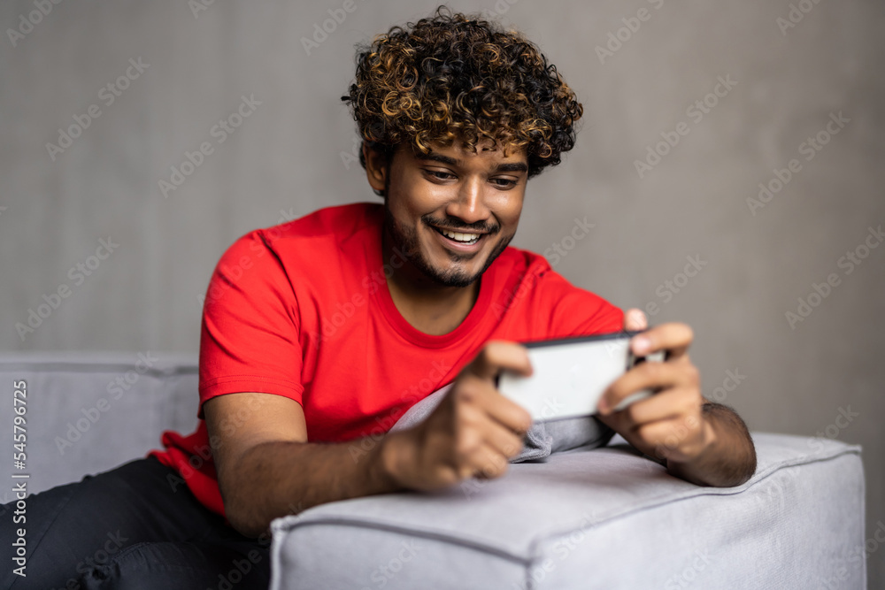 Smartphone social media concept. Indian guy using mobile phone. Asian man relaxed and lying on sofa indoor. Smartphone social media concept. Indian guy using mobile phone. Asian man relaxed and lying on sofa indoor.