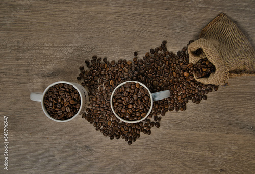 Top view of brown roasted coffee beans spilled on a table with a full coffee mug
