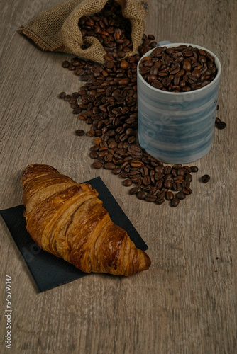 Top view of brown roasted coffee beans spilled on a table with a full coffee mug and biscuit