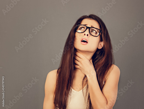 Suffering business woman holding the throat with pain and unhaapy face in eyeglasses looking up on grey copy space background. Waiting the sick leave in office work. Closeup