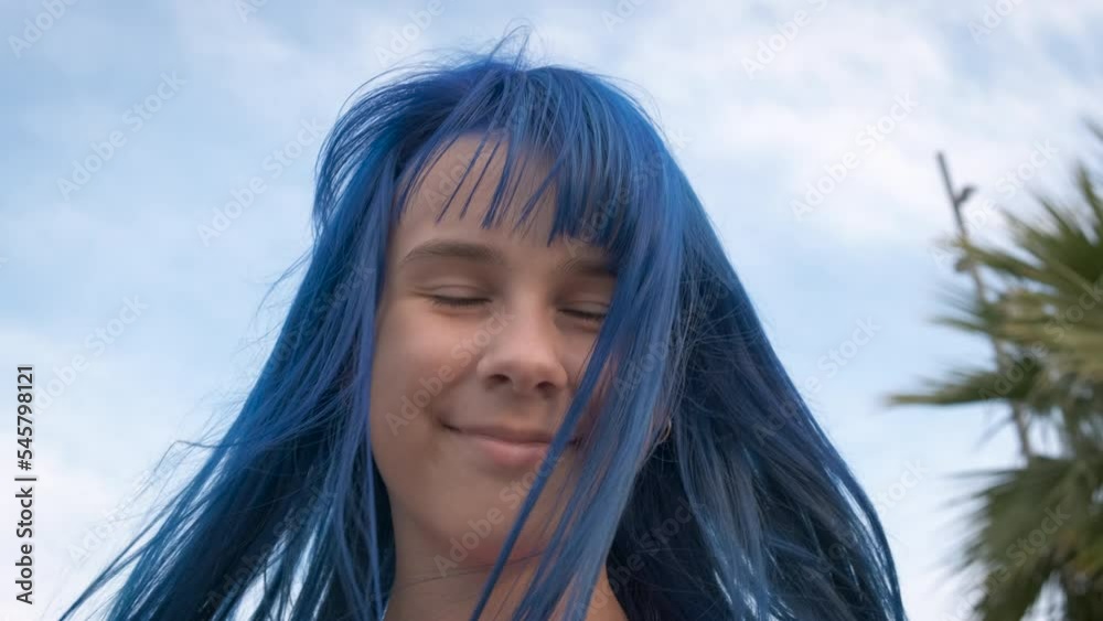 Smiling dyed blue hair girl by sea. A smiling young girl with dyed hairstyle feel the freedom on the shore. A concept of summer tourist and sea resort time. Smiling dyed blue hair girl by sea. A smiling young girl with dyed hairstyle feel the freedom on the shore. A concept of summer tourist and sea resort time.