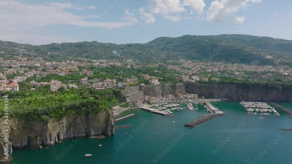 Yachts and sailboats moored in marina. Backwards fly along sea coast. Turquoise water lined with tall rock cliff. Amalfi, Italy Yachts and sailboats moored in marina. Backwards fly along sea coast. Turquoise water lined with tall rock cliff. Amalfi, Italy