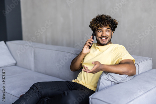 Young indian man talking on the phone while sitting on a couch