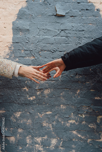 A guy and a girl in autumn clothes want to hold hands against the backdrop of a brick wall.