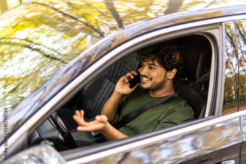 Portrait of young handsome indian man driving car and speaking on mobile phone.