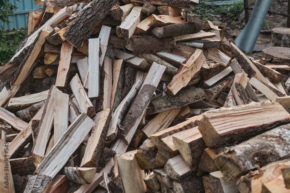 A man worker loads firewood into a wheelbarrow for heating the house which are unloaded in the yard A man worker loads firewood into a wheelbarrow for heating the house which are unloaded in the yard