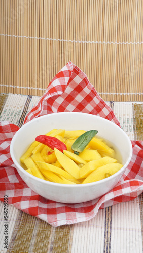 Homemade Manisan or Asinan Mangga is Candied Young Mango Pickles, Thin Sliced Mix with Water and Sugar and then Preserved on a White Bowl. photo