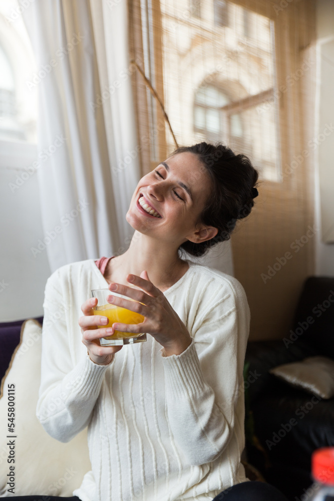 Caucasian woman having orange juice sitting on a sofa indoors feeling cheerful Caucasian woman having orange juice sitting on a sofa indoors feeling cheerful