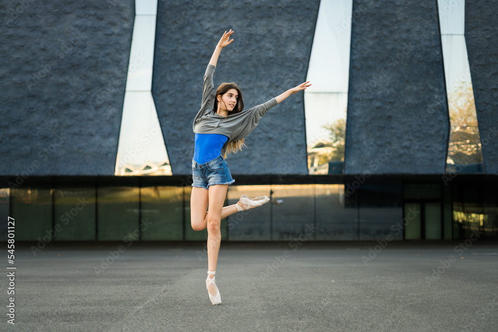 Woman in street clothes and ballerina shoes dancing outdoors on concrete.