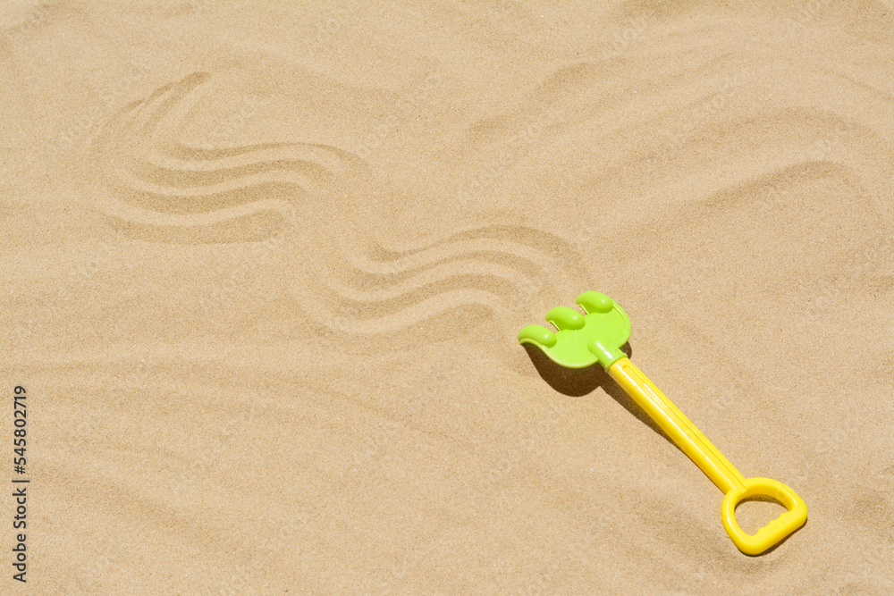 Plastic rake on sand, space for text. Beach toy Plastic rake on sand, space for text. Beach toy