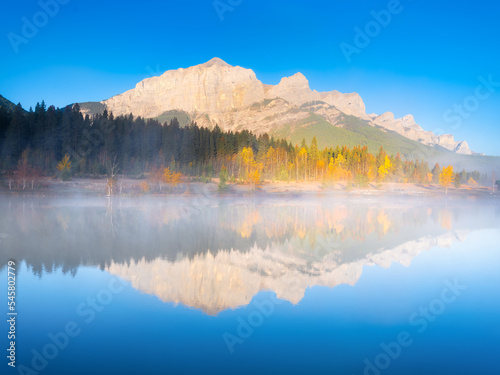 Mountain landscape at dawn. Foggy morning. Lake and forest in a mountain valley at dawn. Natural landscape with bright sunshine. Reflections on the surface of the lake. Alberta, Canada.