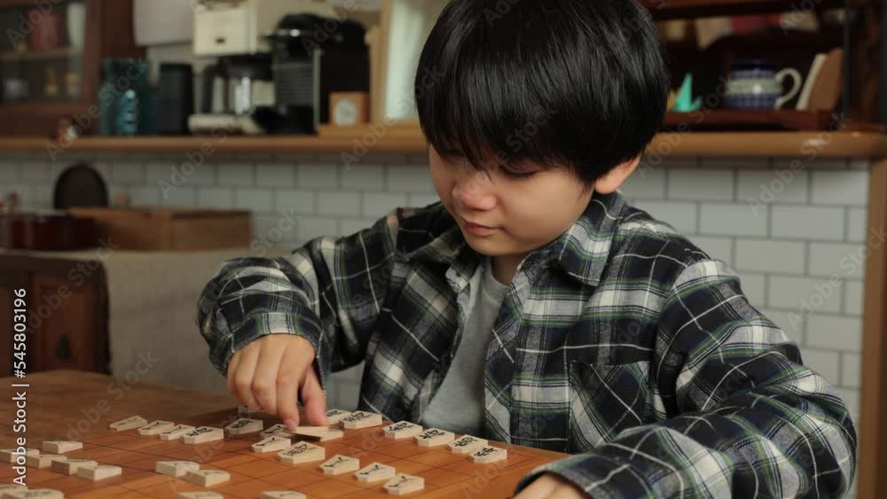 Asian boy playing Shogi game, Japanese chess, at home.