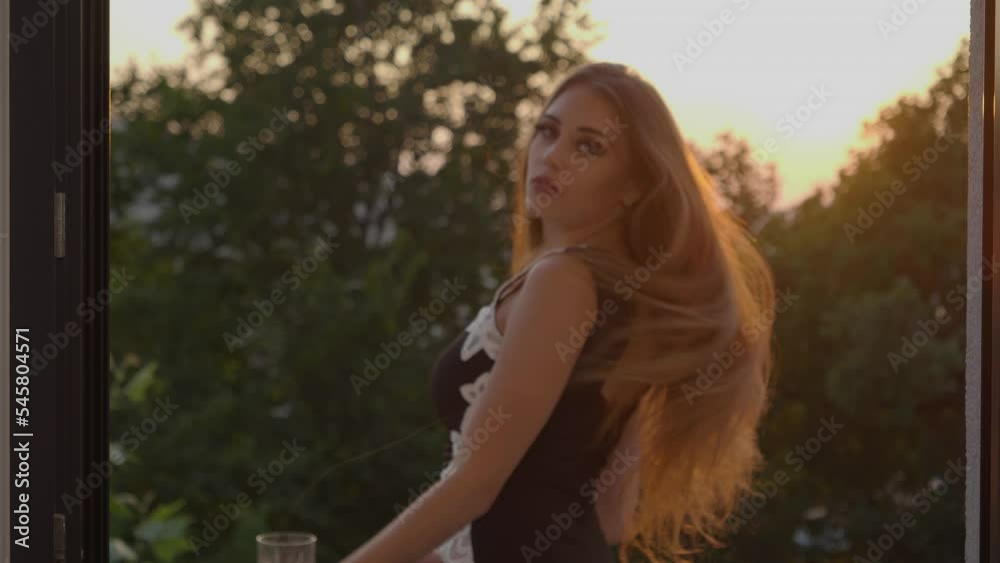 Medium dolly in shot of a beautiful women standing on a balcony at sunset stroking her hair and turning around looking seductively at the camera, slow motion Medium dolly in shot of a beautiful women standing on a balcony at sunset stroking her hair and turning around looking seductively at the camera, slow motion