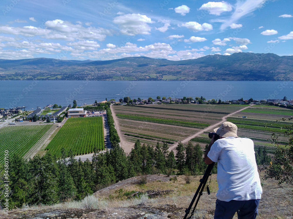 A senior Caucasian white man taking photograph of the landscape overlooking the vineyards and farmland in Okanagan Lake, West Kelowna, Okanagan Valley British Columbia, Canada.
