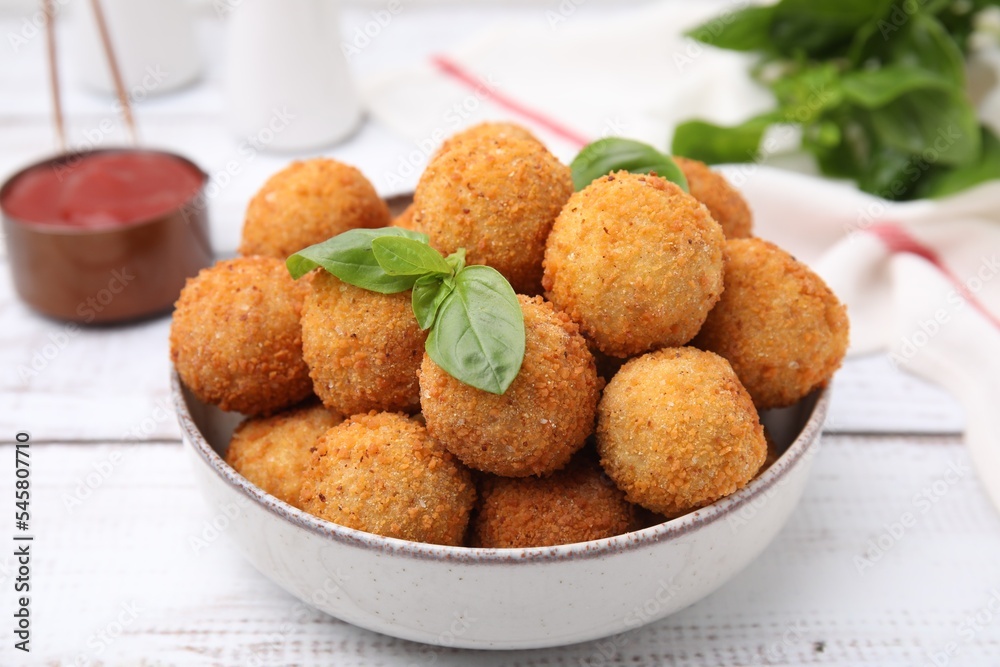 Bowl of delicious fried tofu balls with basil on white wooden table