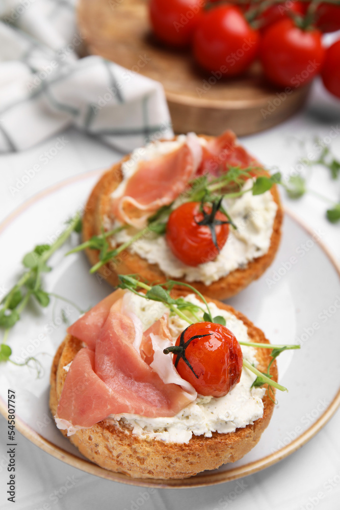 Tasty rusks with prosciutto, cream cheese and tomatoes served on white table, closeup