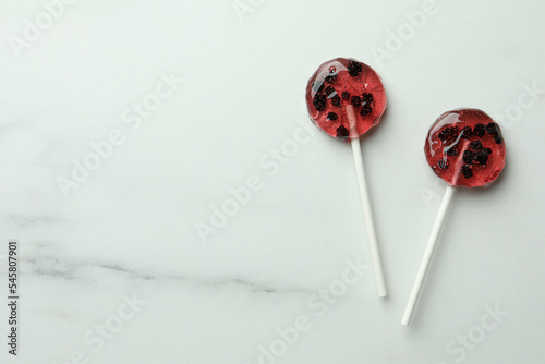 Sweet colorful lollipops with berries on white marble table, flat lay. Space for text